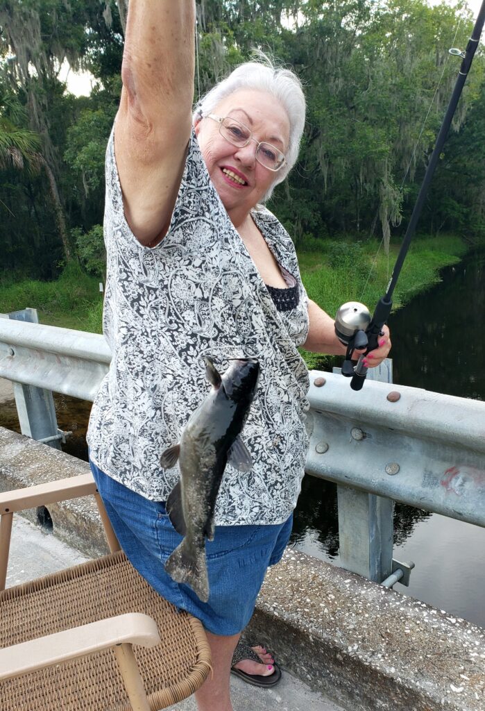 Smiling woman holds a freshly caught fish beside water.